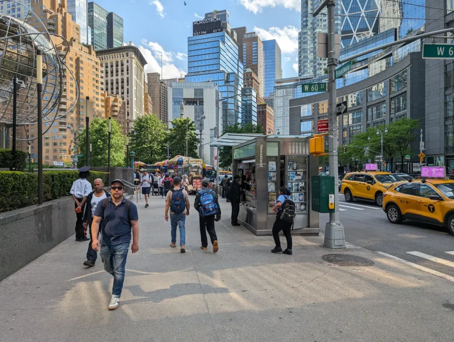 A foto mostra uma rua movimentada de Nova York, com uma banca ocupando apenas uma parte pequena da calçada.