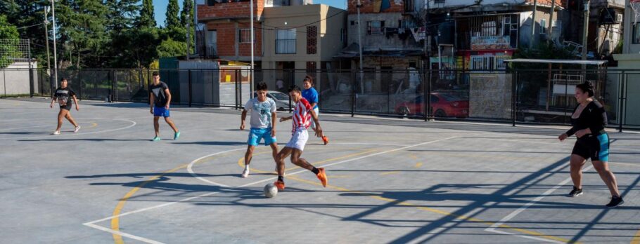 A imagem mostra moradores jogando futebol em um campo recém-construído em Rodrigo Bueno, em Buenos Aires.