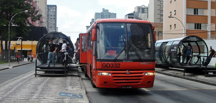 A foto mostra um ônibus numa estação do BRT em Curitiba.